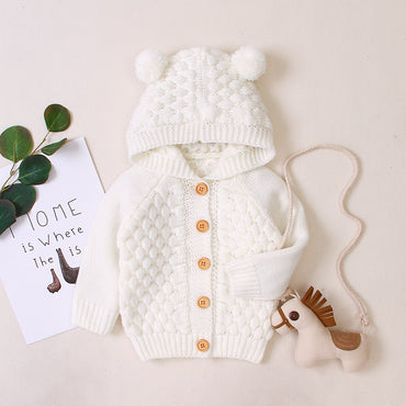 White knitted baby outfit with a hat and cardigan on a light background